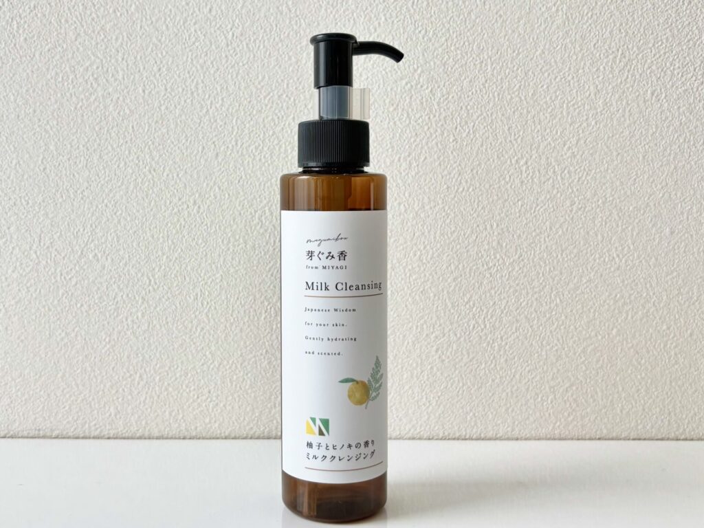 Brown glass pump bottle with a black nozzle on a white label, placed on a white surface against a textured neutral wall.