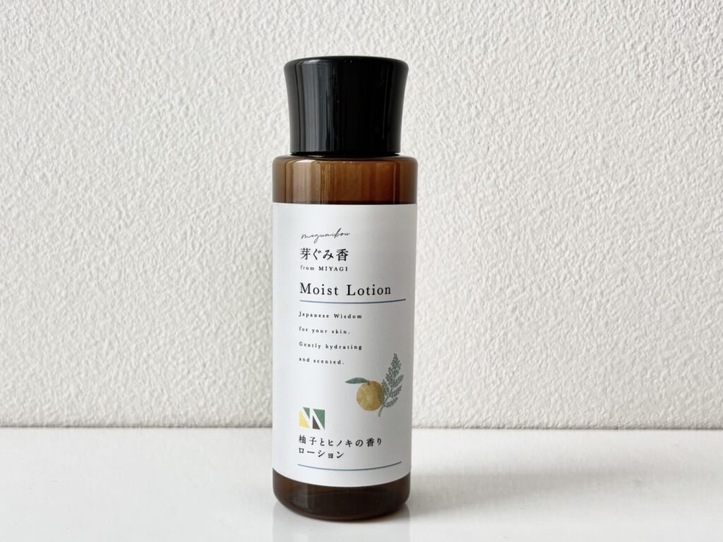 Brown glass lotion bottle with a black cap centered on a white surface; label reads 'Moist Lotion' with Japanese text and small botanical illustration.