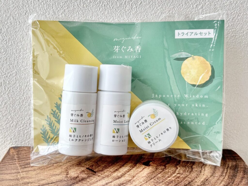 Skincare gift set with three white bottles and a small jar in front of teal-yellow packaging with Japanese text on the label.",